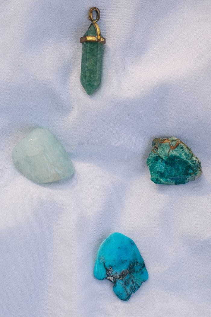 A close-up view of assorted gemstones and a pendant on a smooth fabric surface.